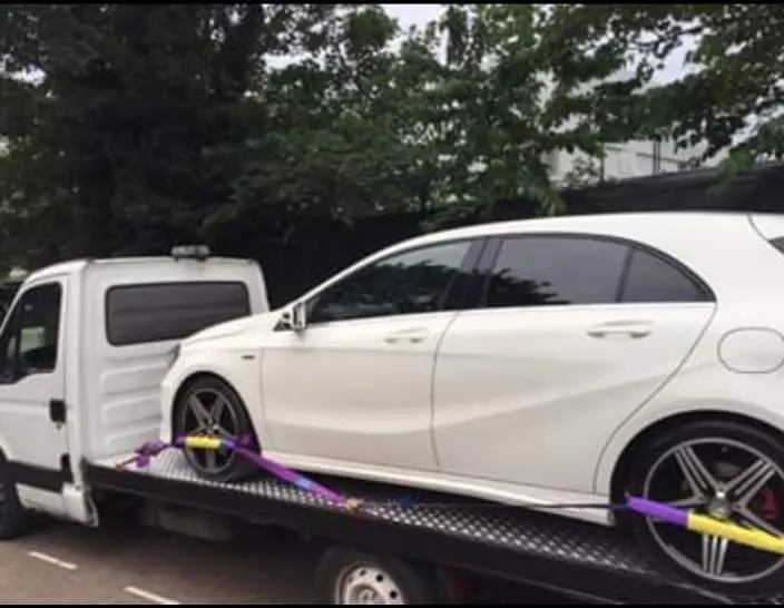 A white car securely placed on a flatbed truck by White Recovery in Kensington W8