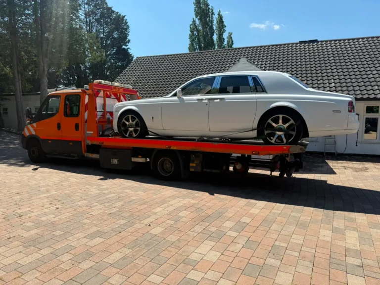 White Rolls-Royce secured on a flatbed recovery truck for safe vehicle transportation.